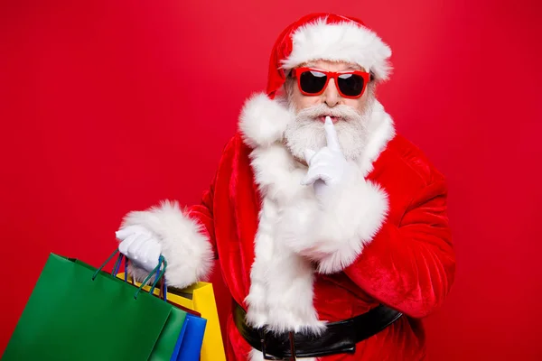 Winter noel eve Christmastime black Friday. Excited hearsay news mature aged grandfather Santa in gloves spectacles white beard package hold forefinger near lips quiet sign isolated red background