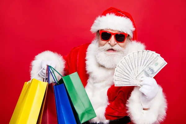 白ひげクリスマス ノエル 月色袋保持赤の背景に分離された Atm 紙幣と眼鏡の伝統衣装に凝ったスタイリッシュなトレンディな成熟した祖父ショッパー ニコラスを高齢者 — ストック写真