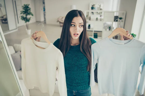 Portrait of pretty beautiful attractive disappointed confused lady trying to choose one sweater color from two holding hangers in hands — Stock Photo, Image