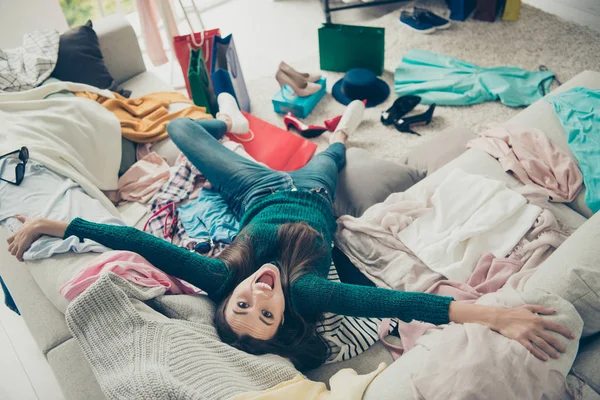 Upside down portrait of nice cute attractive pretty cheerful cheery girl student lying on divan among different things rejoicing having fun in light white interior room