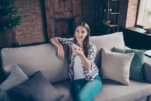 Pretty satisfied cheerful she her lady using remote controller for changing temperature in interior loft room relaxing on beige divan