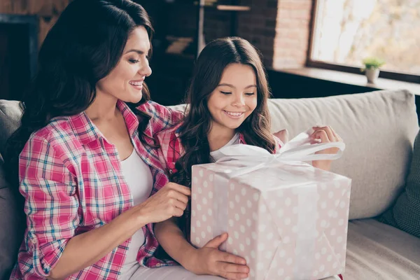 De cerca foto dos personas abrazo mamá hija pequeña satisfecha adorable sentarse con gran caja de regalo 8-marzo fiesta regalo mamá usar camisas a cuadros de color rosa piso apartamento habitación cómodo sofá acogedor diván — Foto de Stock