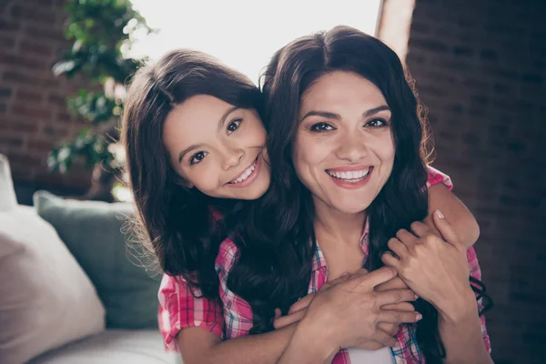 De cerca foto alegre dos personas abrazo mamá pequeña hija satisfecha adorable piggyback celebrar alegre tiempo libre pasar el uso de camisas a cuadros de color rosa piso habitación del apartamento cómodo sofá acogedor diván —  Fotos de Stock