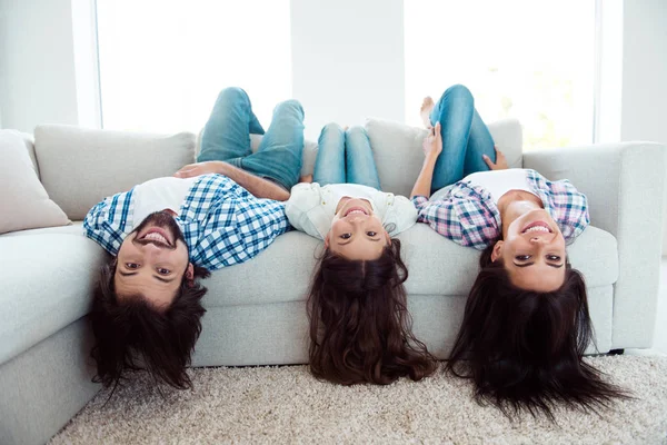 Upside down portrait of nice cute charming attractive cheerful cheery people mom dad lying on divan having fun in light white modern interior indoors