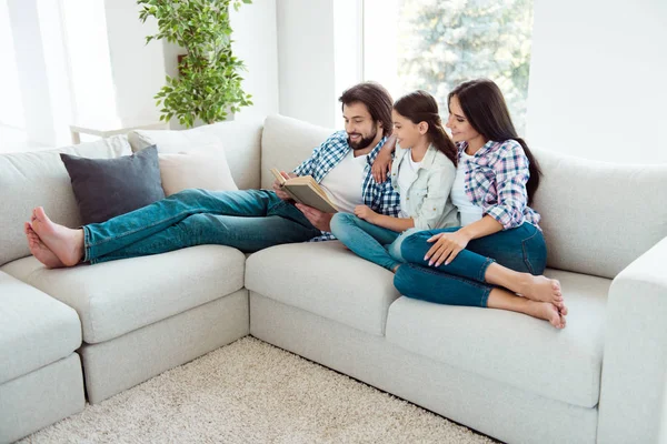 Portret van leuke mooie vriendelijke aantrekkelijke vrolijke vrolijke mensen moeder vader zit op de divan lezen de blote voet sprookjesachtige vrije tijd in lichte witte moderne interieur binnenshuis — Stockfoto