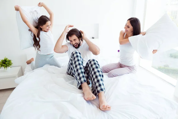 Portrait of nice lovely attractive cheerful cheery crazy glad healthy people sitting on bed enjoying free time fight battle daydream dad daddy mom in white light interior room indoors