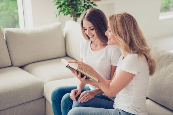 stock image Close up photo of two people mum and teen daughter lovely look to open book holding hands arms adventure novel showing favorite moment wear white t-shirts jeans sit on comfy sofa