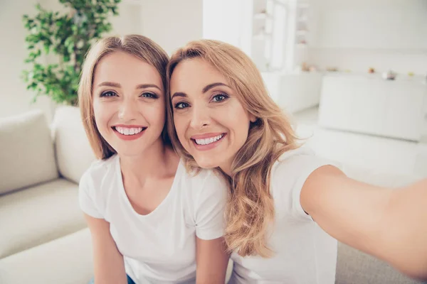 Крупним планом фото двох людей гарненька мама і підліток дочка модний макіяж взяти селфі зубний усміхнений інстаграм блогер одягнути білі футболки джинси сидять на зручному дивані — стокове фото