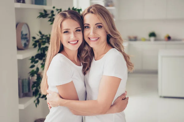 Primer plano foto alegría dentadura sonriendo dos personas mamá y adolescente hija sosteniendo los brazos alrededor del pecho precioso buscando mejores amigos regocijarse usar camisetas blancas jeans en la cocina brillante — Foto de Stock