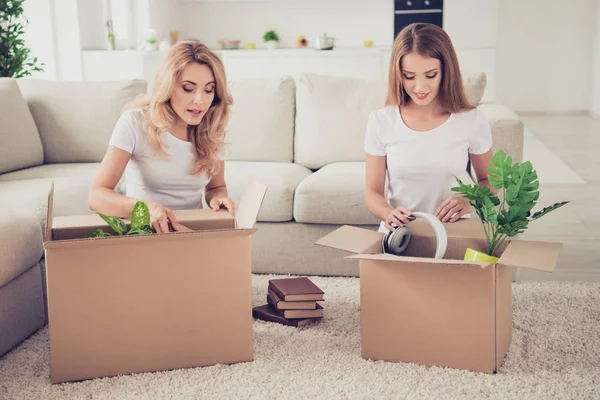 Två fina söt attraktiva vackra winsome charmiga blonda glada glada damer öppna lådor med saker nytt liv inteckning omlokalisering i ljus vit inre rums-hus inomhus — Stockfoto