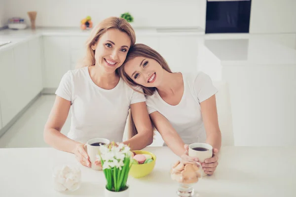 Close-up foto twee mensen mama en tiener dochter huis werk taken drinken thee koffie familie moment hoofd mooie op Mama schouder leunen droeg witte t-shirts jeans in heldere platte keuken — Stockfoto