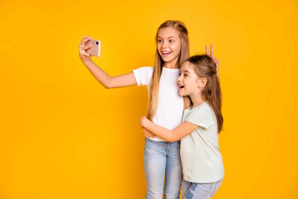 Portret van twee leuke aantrekkelijke mooie vrolijke vrolijke positieve meisjesachtig meisjes tonen van v-sign als Haas oren bedriegt maken selfie geïsoleerd over heldere levendige glans gele achtergrond — Stockfoto
