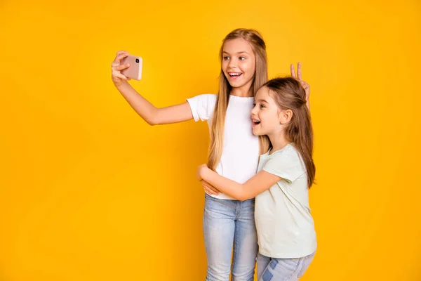 Retrato de dos simpáticas y atractivas chicas alegres alegres y alegres que muestran signos de v como orejas de liebre engañando haciendo selfie aislado sobre brillante brillo vívido fondo amarillo —  Fotos de Stock