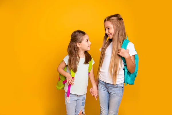 Retrato de dois agradável atraente adorável alegre meninas pré-adolescente alegre com mochilas coloridas segurando as mãos fofocando falar isolado sobre brilhante brilho vívido fundo amarelo — Fotografia de Stock