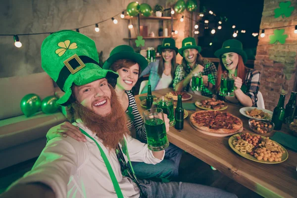 Groupe copains mains bras bière table pizza chips viande culture nationale costumes tradition leprechaun chapeaux casual carreaux carreaux jeans chemises chance barbe rire faire prendre selfies clin d'oeil — Photo