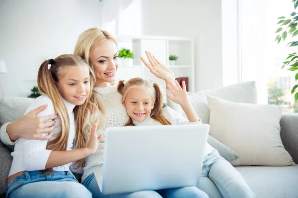 Portrait of three nice cute lovely attractive winsome charming cheerful positive people pre-teen girls mom sitting on divan making video call relatives in light white interior room indoors — Stock Photo, Image