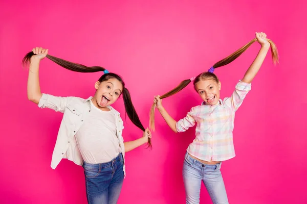 Close-up foto twee vrij beetje leeftijd meisjes vakantie plezier funky kinderachtig blij tong uit de mond kapsel omhoog in de lucht, het dragen van casual jeans denim overhemden geïsoleerd steeg licht levendige bruisende achtergrond — Stockfoto