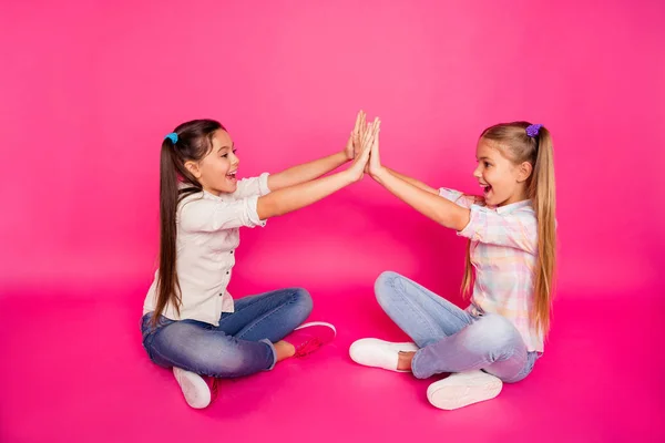 Närbild foto sida profil två lite ålder hon hennes flickor händer armar clap bästa vänner sit golvet ben korsade bär casual jeans denim rutig pläd skjortor isolerade ros pulserande levande bakgrund — Stockfoto