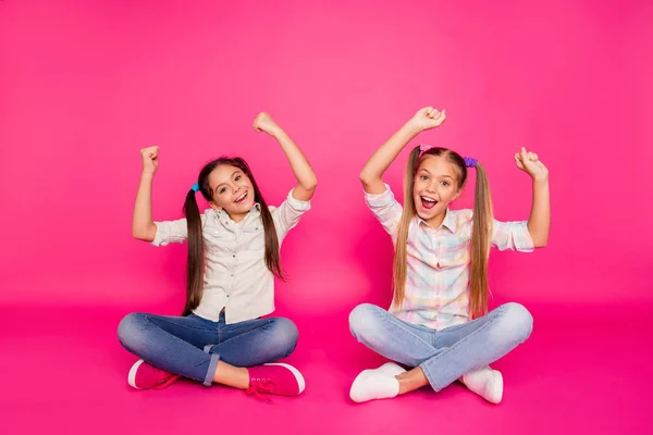 De cerca foto dos poca edad ella sus manos de las niñas brazos hasta mejores amigos se sientan piernas cruzadas ganadores usando vaqueros vaqueros camisas a cuadros aislados rosa vibrante fondo vívido —  Fotos de Stock