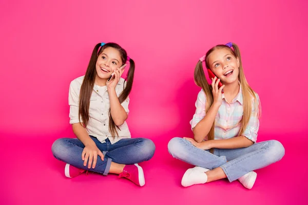 Närbild foto två personer lite ålder hon hennes flickor hålla händer armar telefoner berätta föräldrar nyheter glad sit golvet slitage casual jeans denim rutig pläd skjortor isolerade ros pulserande levande bakgrund — Stockfoto