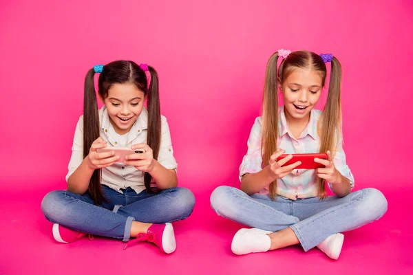 De cerca la foto dos personas de poca edad que sus niñas toman de las manos brazos nuevos teléfonos sentarse adictos a los videojuegos usan vaqueros casuales camisas a cuadros vaqueros aislados rosa rosa vibrante fondo —  Fotos de Stock