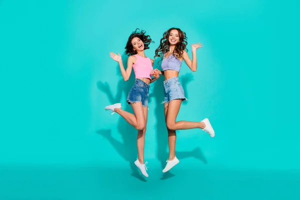 Volledige lengte lichaam grootte foto springen prachtige twee golvende ze haar dames handen armen verhoogd gedag zeggen vriendelijke dragen glimmende jeans denim shorts tanktoppen geïsoleerd teal heldere levendige achtergrond — Stockfoto