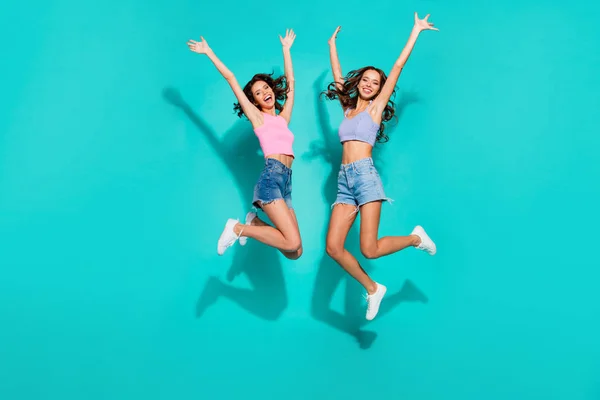 Full length body size side profile photo jumping beautiful funky wavy she her ladies hands up free from duties wearing shiny jeans denim shorts tank tops isolated teal bright vivid background — стоковое фото