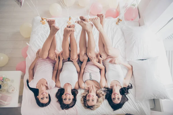 Top above high angle view of nice lovely attractive charming cheerful slim thin fit trendy girlfriends having fun lying on bed rising legs up in light white interior decorated house indoors — Stock Photo, Image