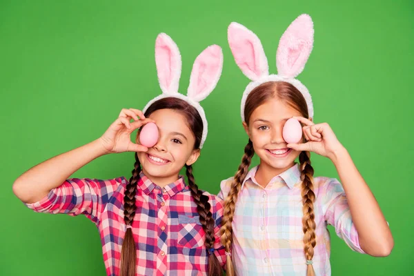 Zbliżenie zdjęcie dwóch dość mało wiek dziewczyny wakacje koncepcja z bunny uszy na ukrywanie głowy jedno oko za Wielkanoc kolorowe jaja sobie dorywczo checkered plaid koszulki na białym tle na zielonym tle — Zdjęcie stockowe