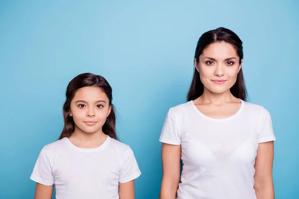 Close up photo amazing two people brown haired mum and small daughter standing straight look like each other wearing white t@-@ shirts isolated on bright blue background — стоковое фото