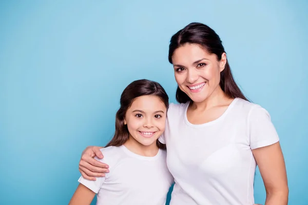 Закрыть фото удивительные красивые два человека каштановые волосы мама маленькая дочь стоять обнимая прекрасный свободное время радоваться носить белые футболки изолированы на ярко-голубом фоне — стоковое фото