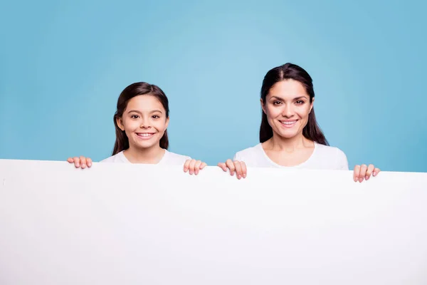 Närbild foto ganska två personer Brun haired mamma lilla dotter toothy strålande leende tom skylt affisch i armar försäljning rabatt bär vita t-shirts isolerade ljusa blå bakgrund — Stockfoto