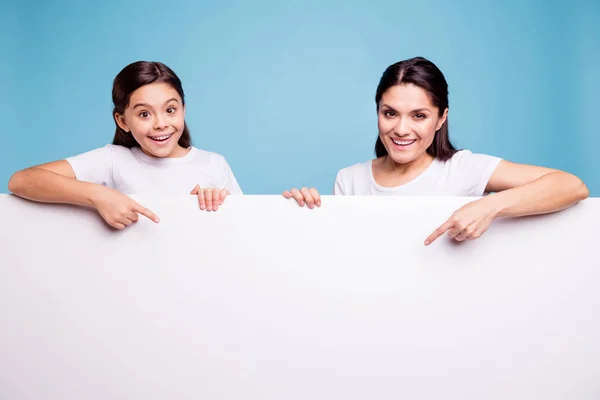 Close up foto bonita duas pessoas de cabelos castanhos mãe pequena filha dedo apontar em cartaz braços segurar cartaz branco venda desconto vestindo camisetas isoladas fundo azul brilhante — Fotografia de Stock