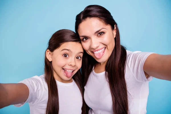 Close up foto animar duas pessoas de cabelos castanhos mãe pequena filha pequena fazer tirar selfies papai esperar ele seu ele ele faltar língua fora da boca desgaste branco t-shirts isolado brilhante azul fundo — Fotografia de Stock