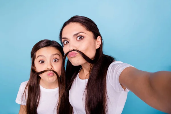 De cerca foto increíble hermosa dos personas de cabello castaño mamá pequeña hija hacer tomar selfies hacer bigote con rizos fingir chico hombre masculino usar blanco camisetas aislado azul brillante fondo —  Fotos de Stock