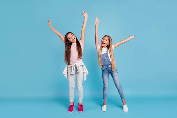Портрет двух симпатичных веселых прямоволосых девочек доподросткового возраста, поднимающих руки вверх, чтобы расслабиться и отдохнуть на голубом бирюзовом фоне — стоковое фото