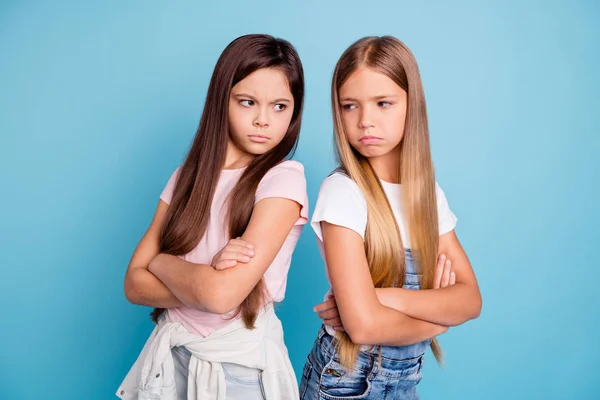 Portrait of two people nice cute lovely attractive sad mad offended gloomy straight-haired pre-teen girls standing back to back folded arms isolated over blue pastel background