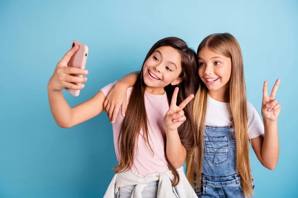 Kapatmak yukarıya fotoğraf iki küçük o onun sarışın esmer kızlar uzun güzel saç telefon olun anne anne göstermek için rahat kot denim t-shirt izole mavi parlak renkli giyen v-sign selfies alır — Stok fotoğraf