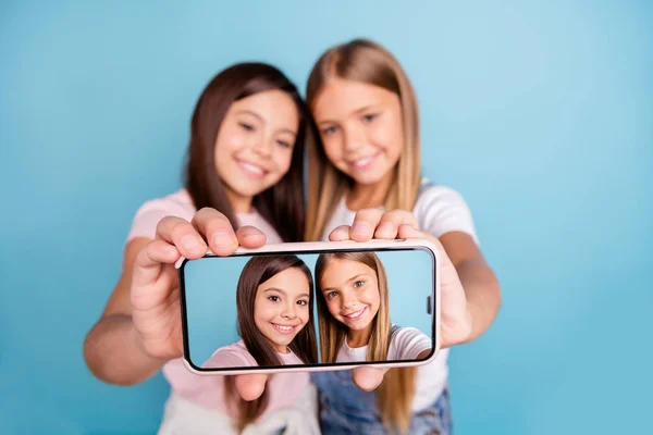 Close up photo two little she her blond brunette girls long pretty hair phone make take selfies instagram followers post wearing casual jeans denim t-shirts isolated blue bright background —  Fotos de Stock