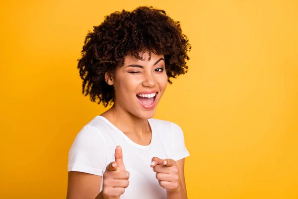 Close up foto piuttosto sorprendente lei la sua pelle scura signora braccia dita puntare su di voi raccogliendo divertente funky ammiccare un occhio ridere risate indossando casual bianco t-shirt isolato giallo brillante vivido sfondo — Foto Stock