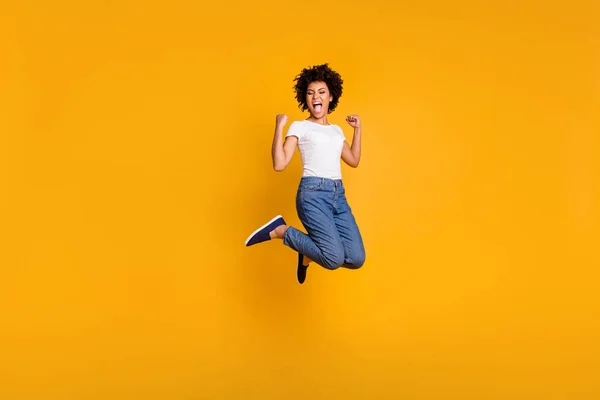 Full length body size side profile photo jumping high beautiful she her lady yelling loud voice hands up win wearing casual jeans white t-shirt clothes isolated yellow bright background — стоковое фото