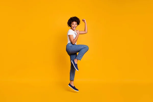 Full length body size side profile photo jumping high beautiful she her lady yelling loud voice legs fsts hands up win wearing casual jeans white t-shirt clothes isolated yellow background — стоковое фото