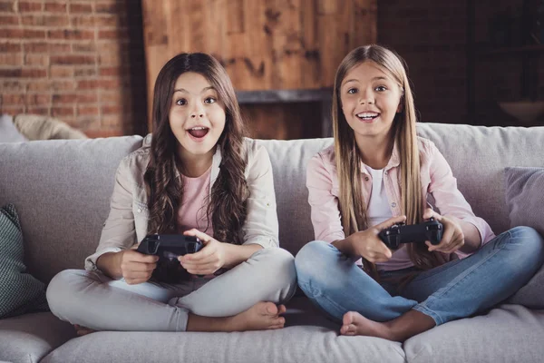 Ritratto di due belle pazze bello attraente affascinante divertente allegro allegro ragazze sedute su divano giocare videogioco dispositivo incrociato gambe in casa loft stile interno industriale — Foto Stock