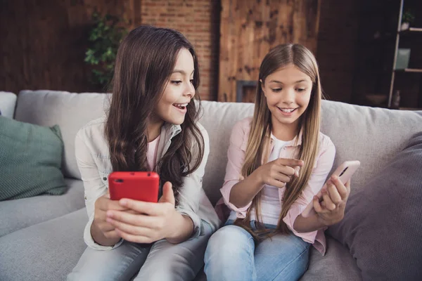 Retrato de cerca de dos hermosas chicas encantadoras encantadoras alegres y alegres dentífricas que usan asientos casuales en diván usando un nuevo dispositivo fresco que muestra la pantalla en el interior industrial del loft de la casa —  Fotos de Stock