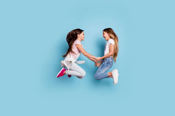 Full length body size side view of two people nice cute attractive cheerful straight-haired pre-teen girls having fun great weekend holding hands isolated over blue pastel background — стоковое фото