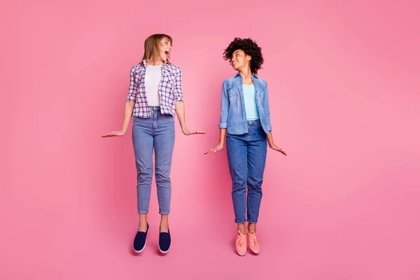 Full length body size view portrait two funky diversity she her ladies good mood jumping high playful childish wear casual jeans denim checkered shirt clothes outfit isolated pink background — Stock Photo, Image