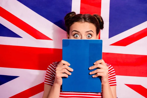 Primer plano retrato de lindo encantador atractivo divertido miedo asustado adolescente chica con rayas camiseta bachelor master grado escondido detrás de libro de texto aislado sobre fondo de la bandera británica — Foto de Stock