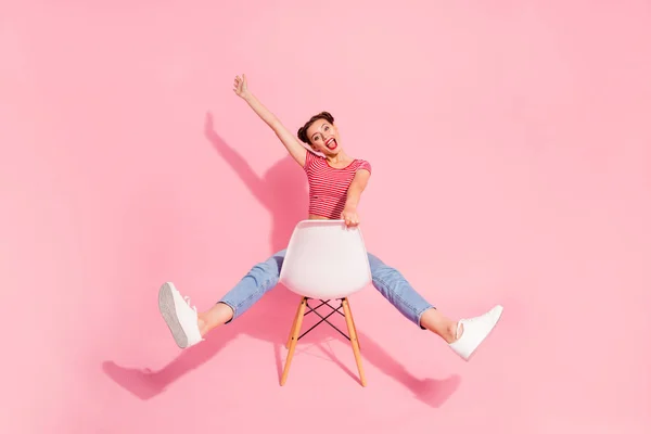 Agradável atraente glamourosa adorável brilho alegre menina otimista alegre vestindo jeans tshirt listrada sentado na cadeira se divertindo levantar a mão isolada sobre fundo pastel rosa — Fotografia de Stock