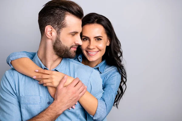 Um caso amoroso. Retrato de casal encantador de millennial alegre positivo colocando as mãos em torno do peito ondulado cabelo encaracolado vestindo camisas jeans azuis isolados no fundo cinza — Fotografia de Stock