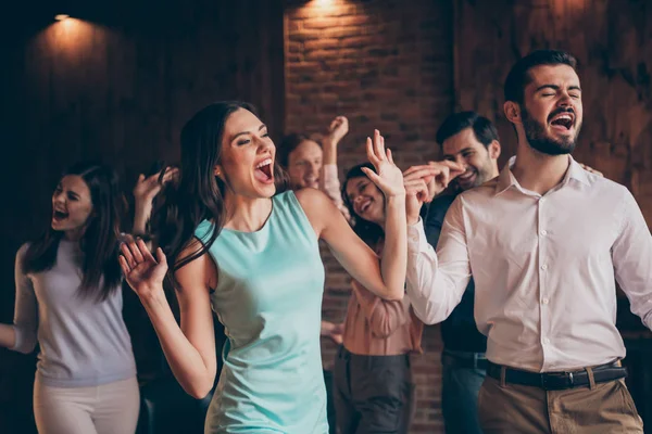 Close up photo classy gathering hang out dance singing look watch see karaoke words screen yell scream shout she her ladies he him his guys wear dress shirts formal wear sit sofa loft room indoors